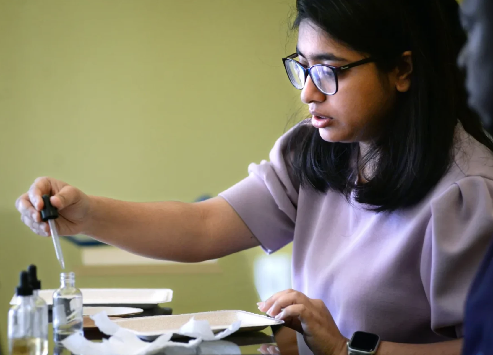 Nabanita Das, a student in the University of Maine's School of Forest Resources, puts drops of oil ontp a paper plate with a pulp-based coating to show how it prevents the oil from soaking in. Das and a group of University of Maine, Orono, researchers are developing alternatives to the unhealthy PFAS coatings that had been used to keep oil from soaking into single-use paper plates.